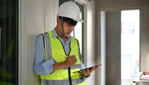 Asian male engineer in safety helmet using digital tablet, checking building construction progress.