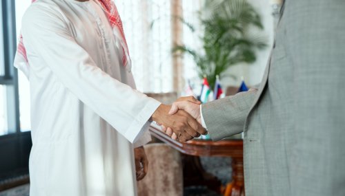 Successful Arabian businessman in national attire greeting his foreign partner by handshake after negotiating and making business deal